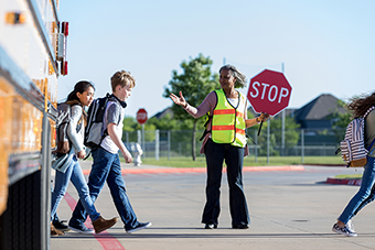 Crossing guard directing kids in front of school bus