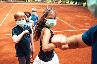 Masked tennis students elbow-bumping instructor