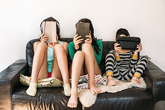 Three kids on iPads sitting on the couch