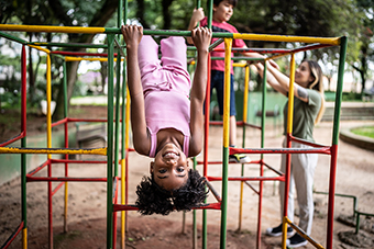 Little girl hanging upside down on a jungle gym